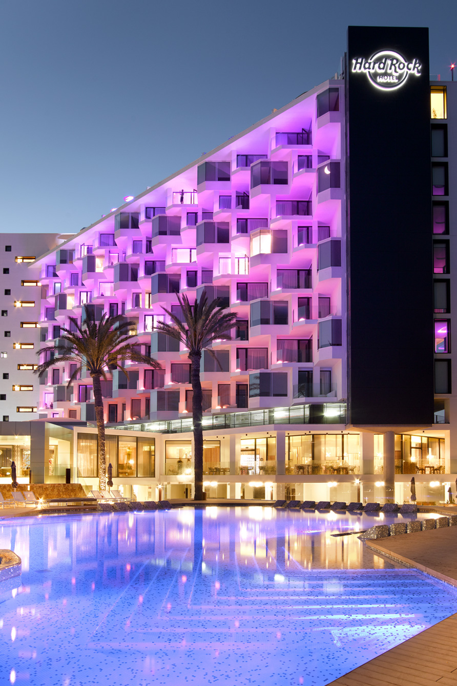 Hard Rock Hotel exterior lit with pinkish hues overlooking pool in the evening.